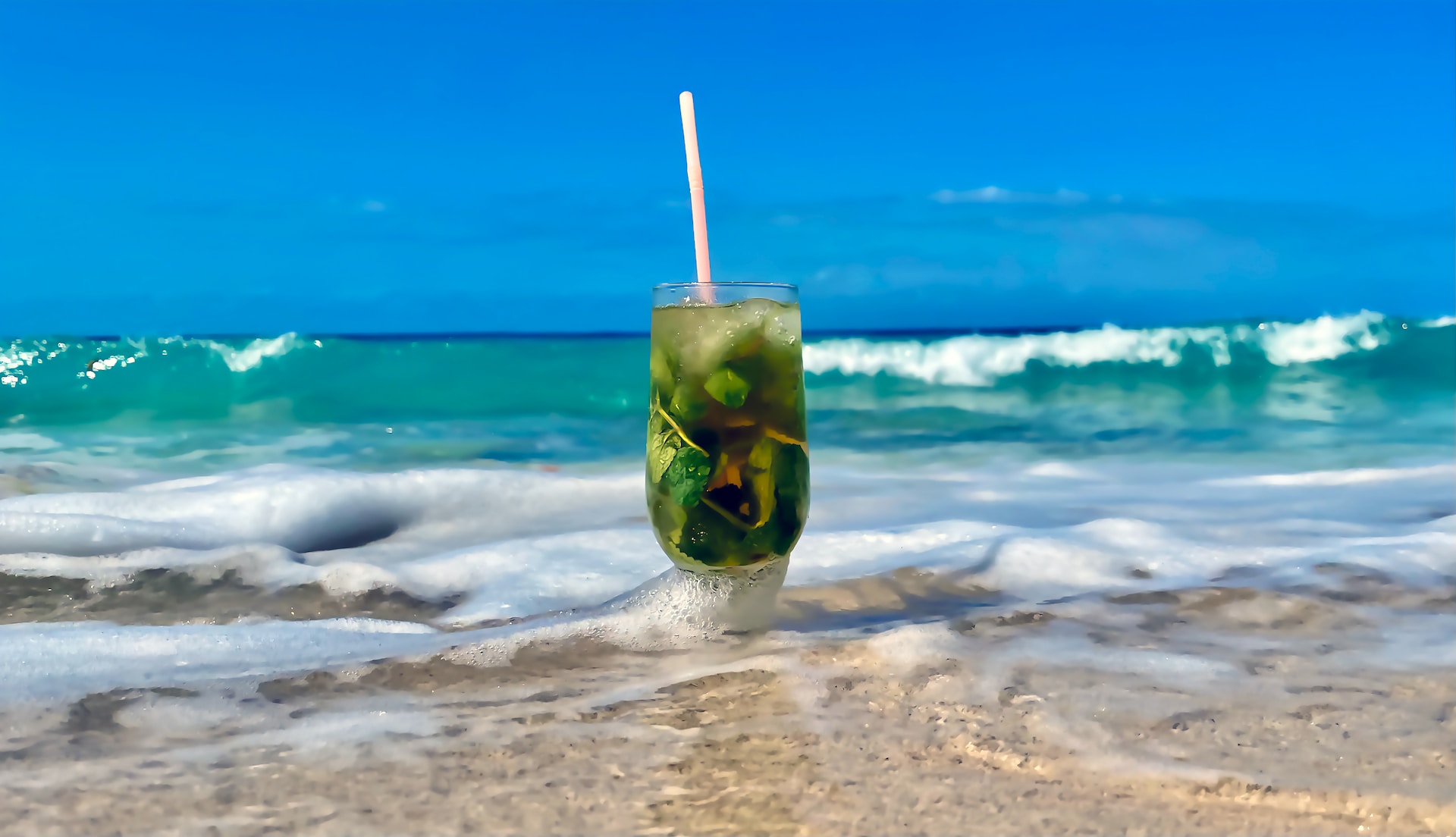 cocktail sitting on beach as waves roll in