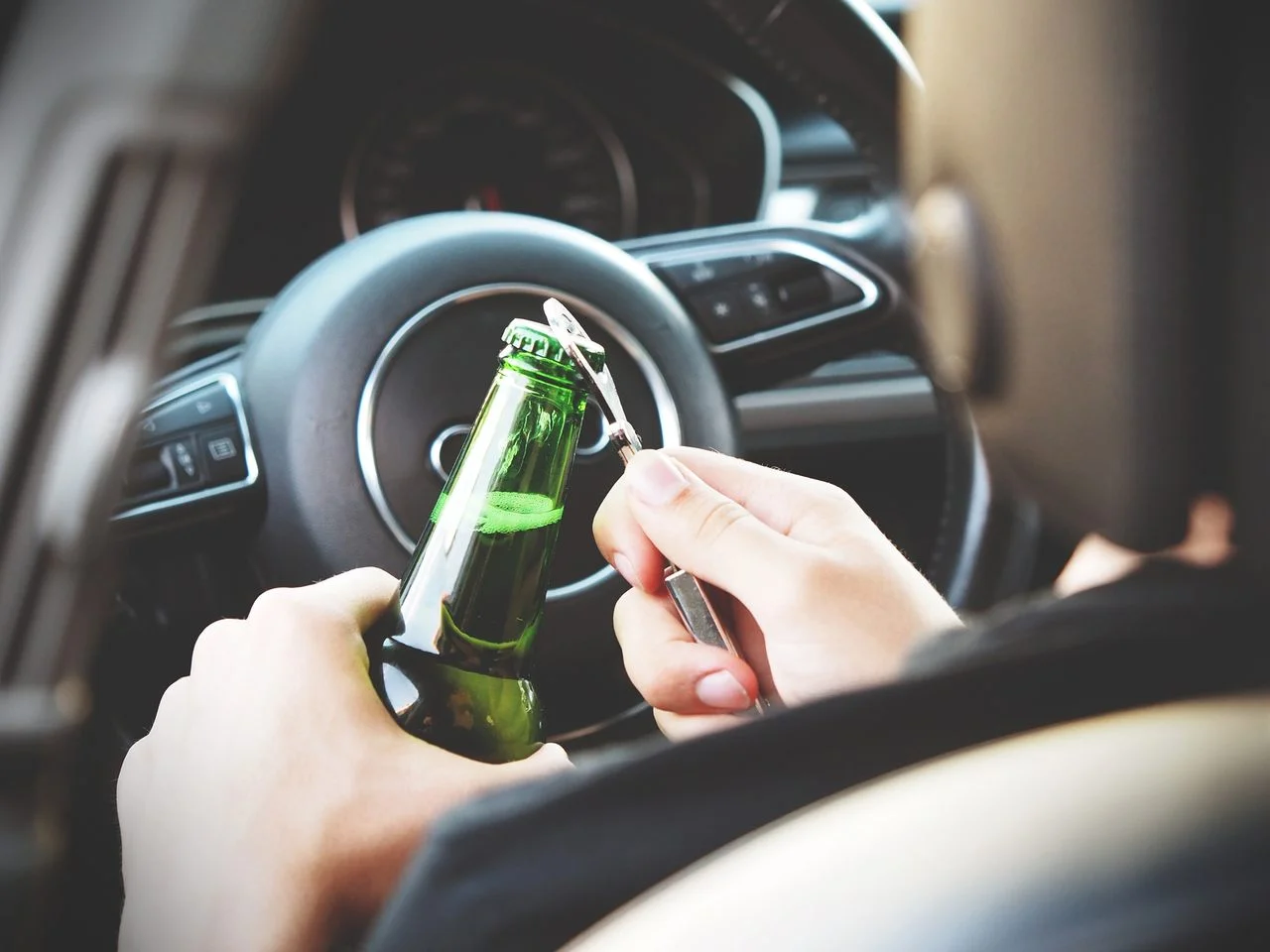 man opening beer bottle while driving