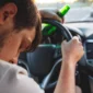 Person sleeping against steering wheel with beer bottle in hand