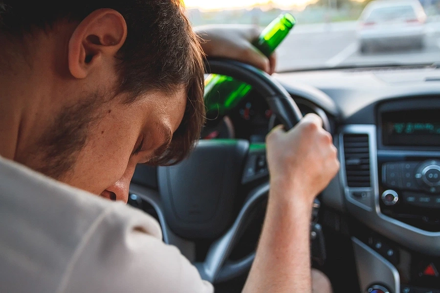 Person sleeping against steering wheel with beer bottle in hand